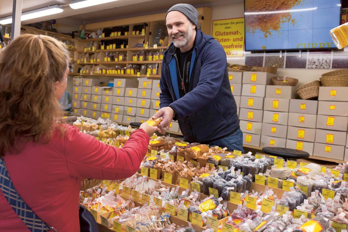 Ein Verkäufer überreicht einer Frau ein Gewürzpackung an einem Stand auf der Haefelesmess
